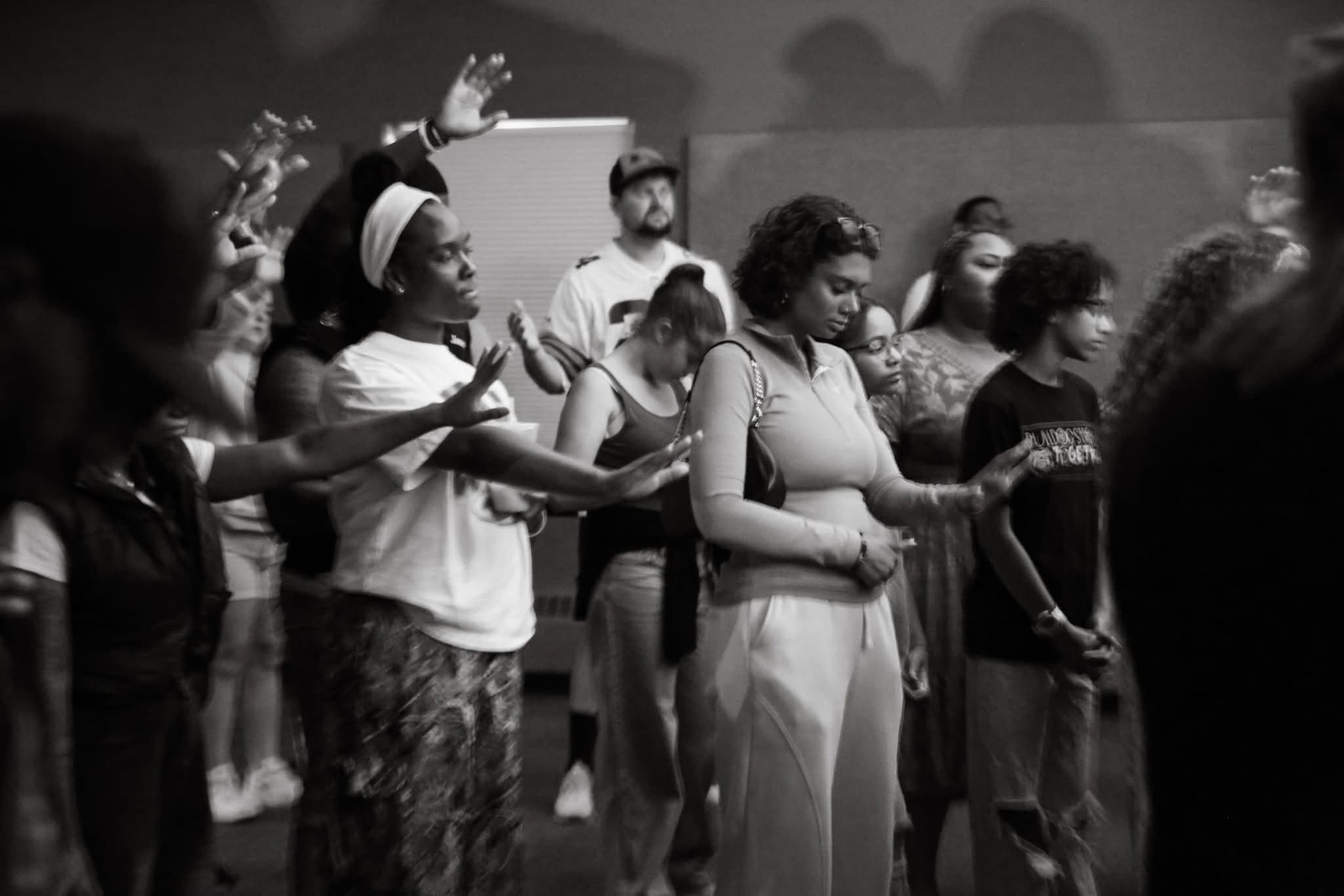 Black-and-white photo of the crowd at Summer Glory in worship, eyes closed and hands extended in prayer.