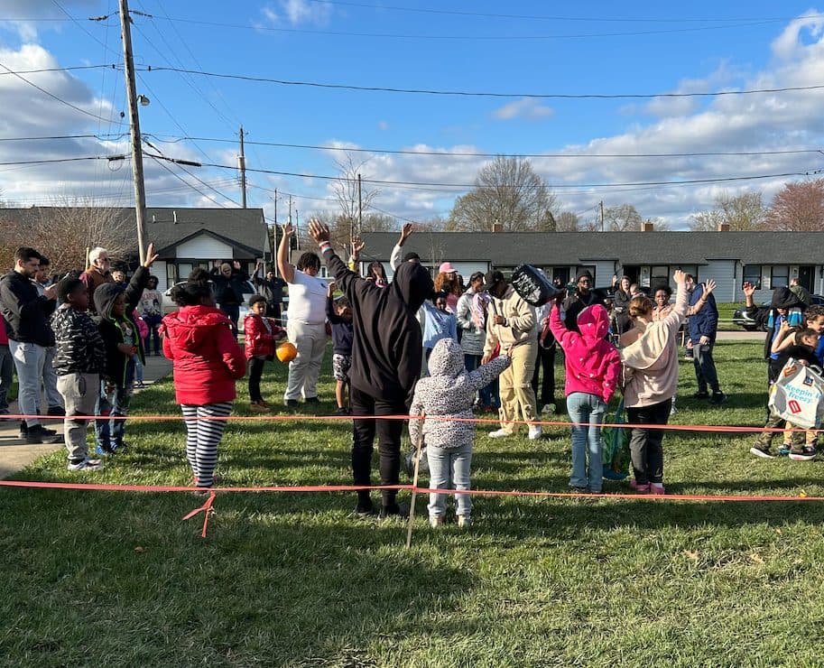 Kids and adults raise their hands in worship at an outdoor community gathering.