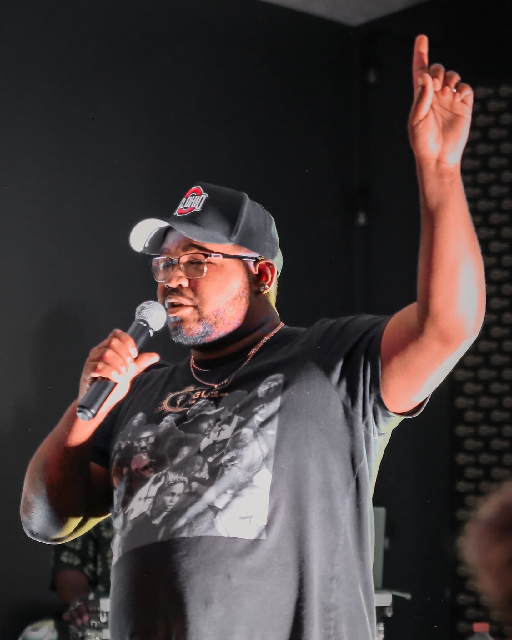 Geo Preston on stage at the Summer Glory Concert, speaking into a microphone and pointing up.